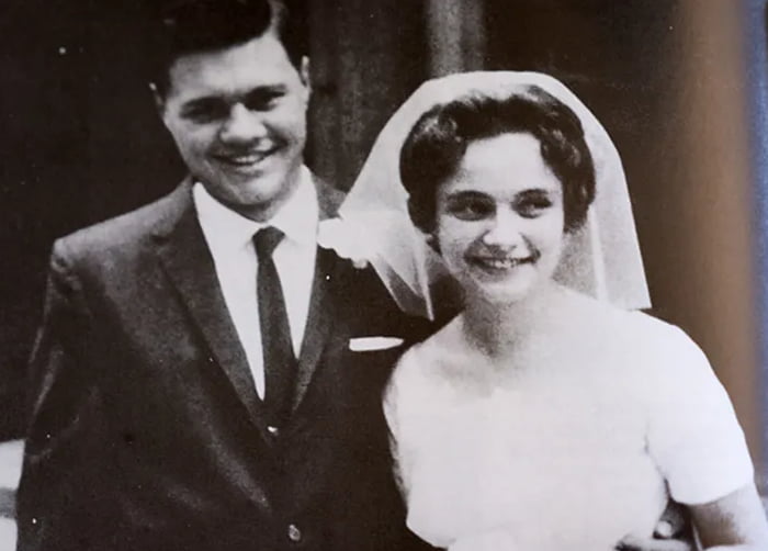 Foto preta e branca do casamento de Tom e Margie Monaghan. Ele de terno e ela com vestido de noiva.